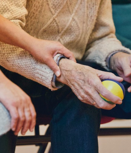 women holding elderly womens arm while doing physio exercises with a small ball